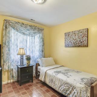 A cozy bedroom with a single bed, yellow-painted walls, and a window adorned with floral curtains.