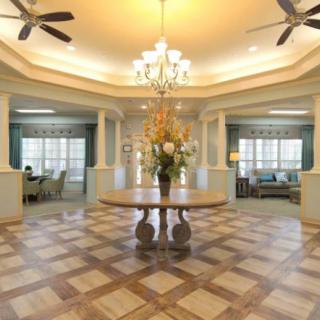 An elegant living room with a decorative wooden floor, featuring a central table adorned with flowers under a chandelier.