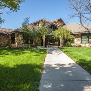 A beautiful residential house with a well-maintained lawn and trees under a clear blue sky.