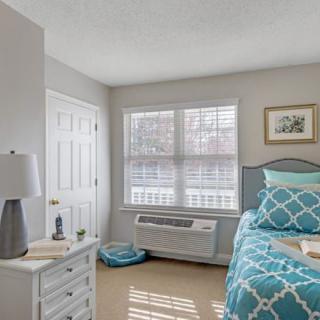 A cozy bedroom with a neatly made bed, bedside table, and a window letting in natural light.