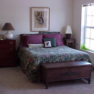 A cozy bedroom featuring a comfortable bed with decorative pillows, lamps on either side, and a window allowing natural light to fill the space.