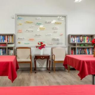 A cozy reading room with bookshelves, red-covered tables, and chairs.