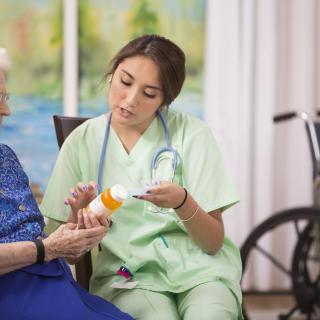 A nurse in scrubs is discussing medication with an elderly woman in a healthcare setting.