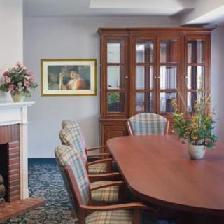 A well-furnished conference room with a wooden table, chairs, and a cabinet with glass doors. A fireplace is on the left with artwork hanging above it.