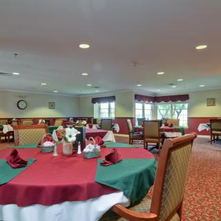 A spacious dining room with tables set for a meal, featuring red and green tablecloths.