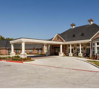 A large building with a covered entrance and columns, surrounded by landscaped grounds.