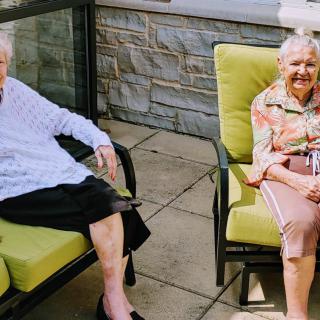 Two elderly women sitting and relaxing on outdoor patio chairs.