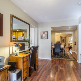 A cozy interior view showcasing a home office setup alongside a living and dining area with hardwood flooring.