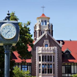 A scenic view of a historic building with a red roof and gothic architecture, accompanied by a street clock.
