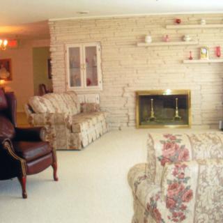 A cozy living room featuring a brick fireplace, floral patterned furniture, and an armchair.