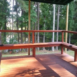 A wooden deck with built-in seating overlooks a tranquil forest area, bathed in sunlight.
