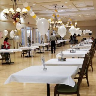 A spacious dining hall set up for an event, featuring neatly arranged tables adorned with white tablecloths and decorative balloons.