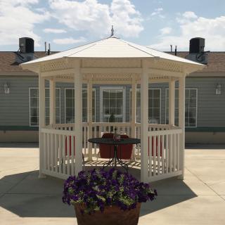 A white gazebo on a sunny day, surrounded by potted flowers.