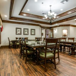 A spacious dining room with elegant wooden flooring, furnished with multiple tables and chairs, adorned by a chandelier and wall art.