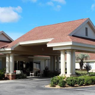 A building with a covered entrance supported by columns and surrounded by landscaping.