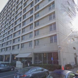 A city street view featuring a multi-story apartment building with parked cars.