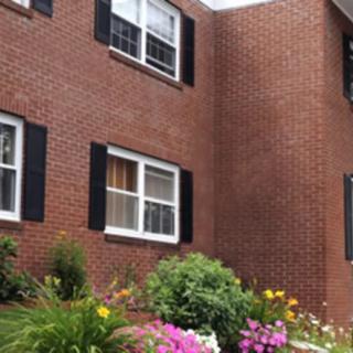 A brick house with black shutters, featuring a colorful garden in the foreground.