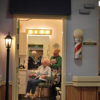 A cozy barbershop with a person receiving a haircut while sitting in a chair, under the warm glow of lights.