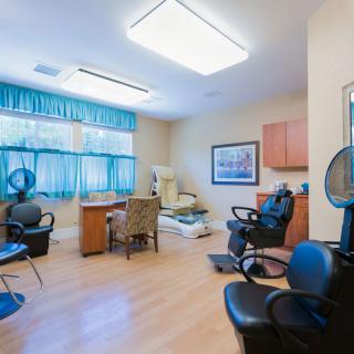 The image shows the interior of a hair salon with styling and dryer chairs, a wooden floor, and large windows.