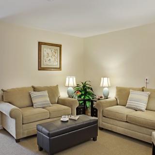 A cozy living room with beige sofas, a dark coffee table, and ambient lighting from side lamps.