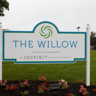 A welcoming sign for The Willow at Inspirit, surrounded by colorful flowers.