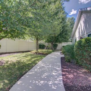 A sunny sidewalk lined with trees and bushes leading to a house.