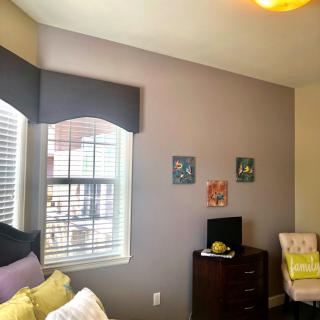 A cozy bedroom with a window, dresser, and wall art.
