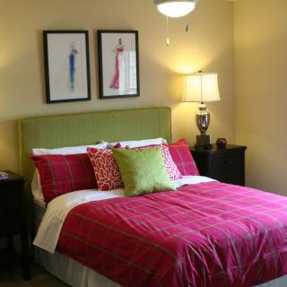 A cozy bedroom featuring a neatly made bed with vibrant pink bedding, decorative pillows, and artwork on the wall.