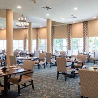 A spacious and elegantly decorated dining area with multiple tables and chairs, featuring large windows and ambient lighting.