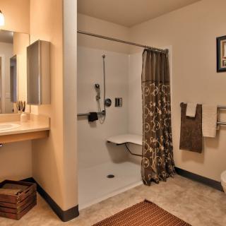 An accessible bathroom featuring a shower with a seat, sink, and towel rack.
