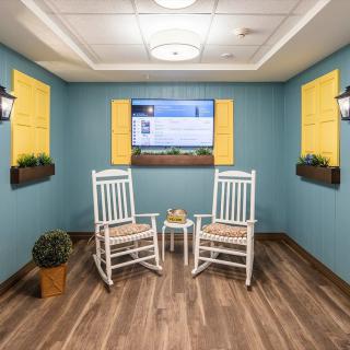 A cozy room with two white rocking chairs facing a wall-mounted television, accented by blue walls and yellow shutters.