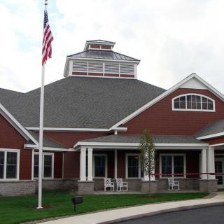 A red brick building with an American flag in front, featuring a covered entrance and multiple windows.