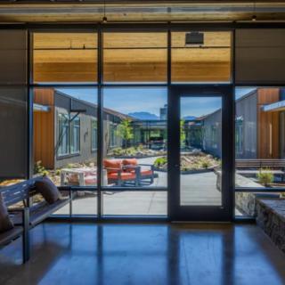 A modern interior space with large glass doors opening to a courtyard featuring outdoor seating and landscaping.