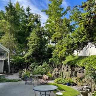 A serene garden with lush greenery, featuring tables and chairs under a clear blue sky.
