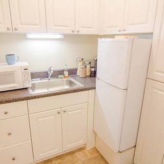 A compact kitchen with white cabinets, featuring a microwave, refrigerator, and sink.