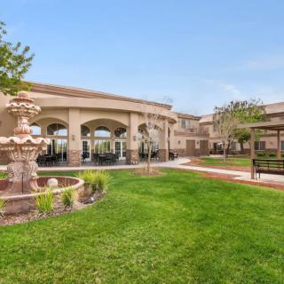 A spacious garden with a fountain and benches in front of a large building.