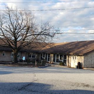 A quaint building surrounded by a large tree under a cloudy sky.