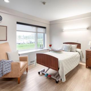 A clean and well-lit hospital room with a bed, chair, and window, creating a calm healthcare environment.