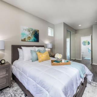 A modern and stylish bedroom featuring a neatly made bed with accent pillows, an artwork on the wall, and a nightstand with lamps.