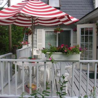 A cozy patio area with a red and white striped umbrella, surrounded by flowers and outdoor seating.
