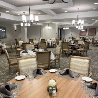 An elegantly set dining room with multiple tables and chairs, decorated with chandeliers and place settings.