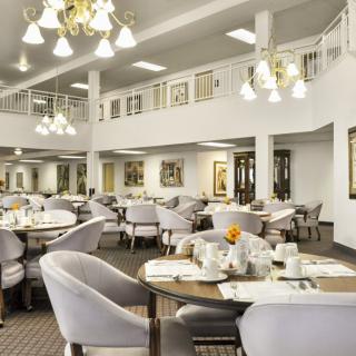 An elegant dining area featuring well-set tables and comfortable chairs under ornate chandeliers.