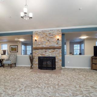 A spacious living room with a central stone fireplace, carpeted flooring, and elegant furniture.