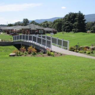 A scenic view of a garden with a bridge leading to a building, surrounded by lush greenery and hills in the background.