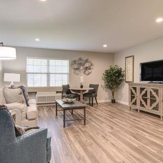 A modern living room with cozy seating, wood flooring, and a small dining area.