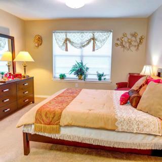 A cozy and well-decorated bedroom with a large bed, lamps, and plants by the window.