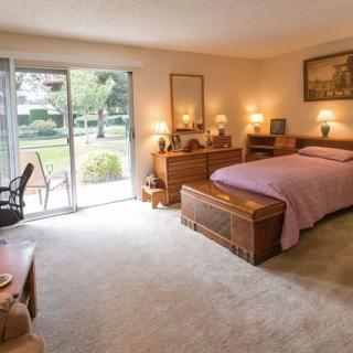 A cozy bedroom with a large bed, wooden furniture, and a sliding door opening to a garden view.