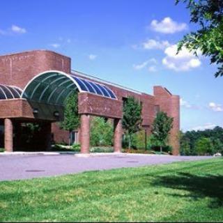 A modern architectural building surrounded by greenery under a clear blue sky.