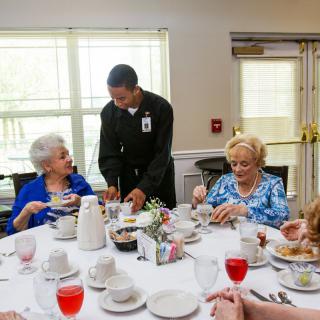 A waiter serves a meal to a group of elderly individuals dining together.