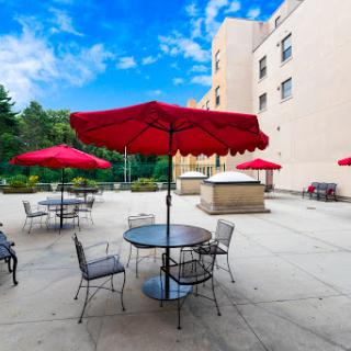 A relaxing outdoor patio area with red umbrellas providing shade over tables and chairs, set against a bright blue sky.
